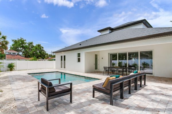 WinWay Homes Geometric In-Ground Pool with Sleek Design and Chairs, Covered Patio & Dining Area Behind White Modern Home