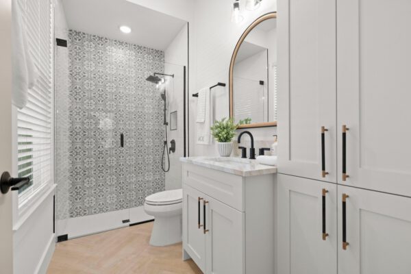 WinWay Homes Bathroom with White Vanity, Patterned Shower Wall, White Cabinetry, Curved Mirror & Black Fixtures