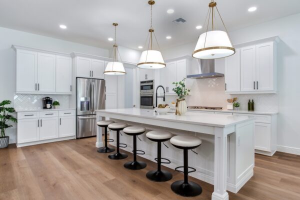 WinWay Homes Open-Concept Kitchen with large white island, pendant lights, white cabinetry, stainless appliances & light wood-look flooring