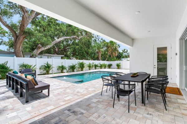 WinWay Homes Covered Outdoor Living Area with Dining Table, Pool View, Paver Flooring & White Exterior Walls