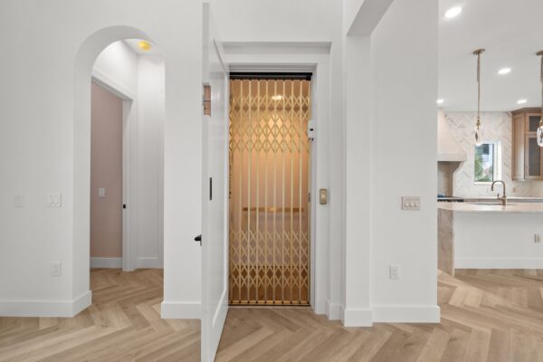 WinWay Homes Hallway with Elevator Door, Arched Opening, Herringbone Flooring, White Walls & Open Kitchen View