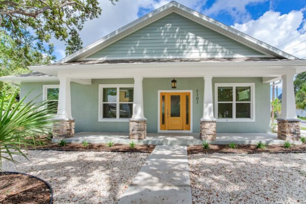 WinWay Homes Pale Green House with Columned Porch, Stone Accents, White Trim, and Yellow Door