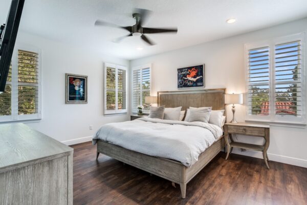 WinWay Homes Primary Bedroom with Wood-Look Flooring, Ceiling Fan, Plantation Shutters, Upholstered Bed & Neutral Coastal Finishes
