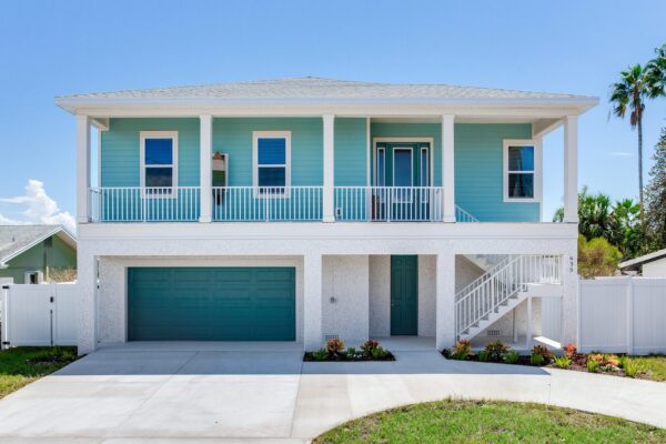 WinWay Homes Elevated Coastal Home With Aqua Siding, Upper Balcony, White Staircase, Teal Garage Door & White Trim