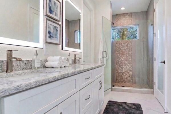 Spa-Style Bathroom with White Double Vanity with Quartz Countertop, Mirrors with Built-in Lighting and Mosaic Shower with Built-in Windo
