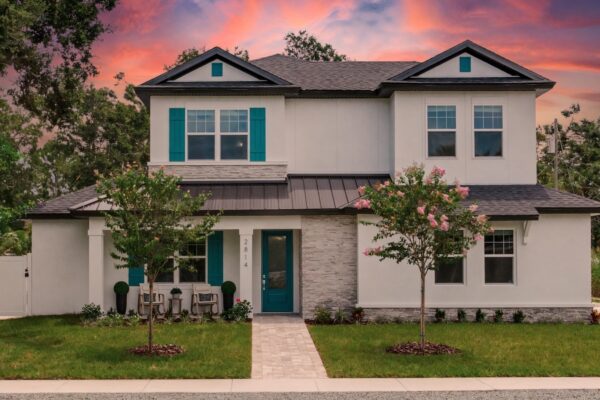 WinWay Homes 2-Story Coastal Home at Sunset with Teal Shutters, Covered Entry, White Exterior, Stone Accents & Attached Garages