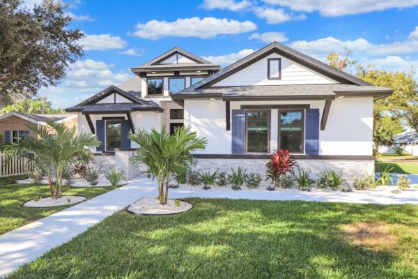 WinWay Homes 1-Story Coastal Home With White Stucco, Dark Trim, Covered Entry, Tropical Landscaping & Front Lawn