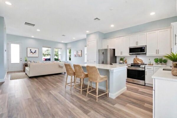 WinWay Homes Open Kitchen and Living Area with Peninsula Seating, White Cabinetry, Light Flooring & Pale Blue Walls