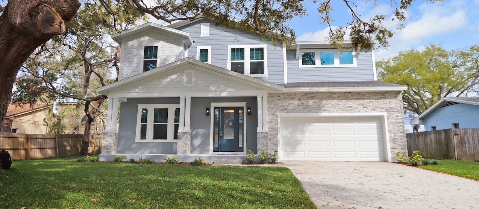 Exterior View of New Cottage Style Home by WinWay Homes in Pale Gray, White Trim, and Columned Porch with Stone Accents Under a Tree