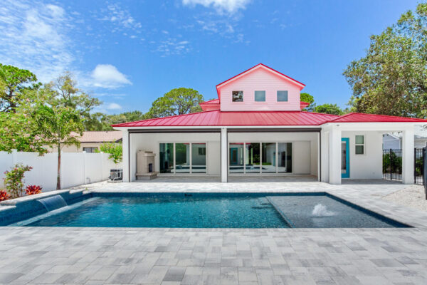 WinWay Homes Rear Exterior with pool, coral roof, covered patio, sliding glass doors & white coastal-style exterior