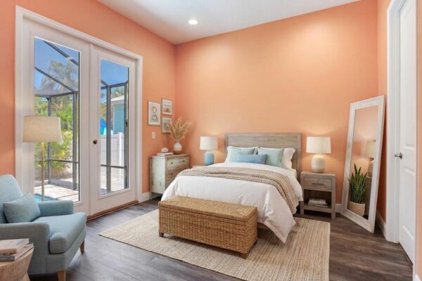WinWay Homes Primary Bedroom with Coral Accent Walls, French Doors, Woven Bench & Light Tile Flooring