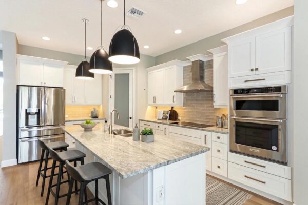 WinWay Homes Kitchen With Large Island, Black Pendant Lights, White Cabinetry, Double Wall Ovens & Stainless Range Hood