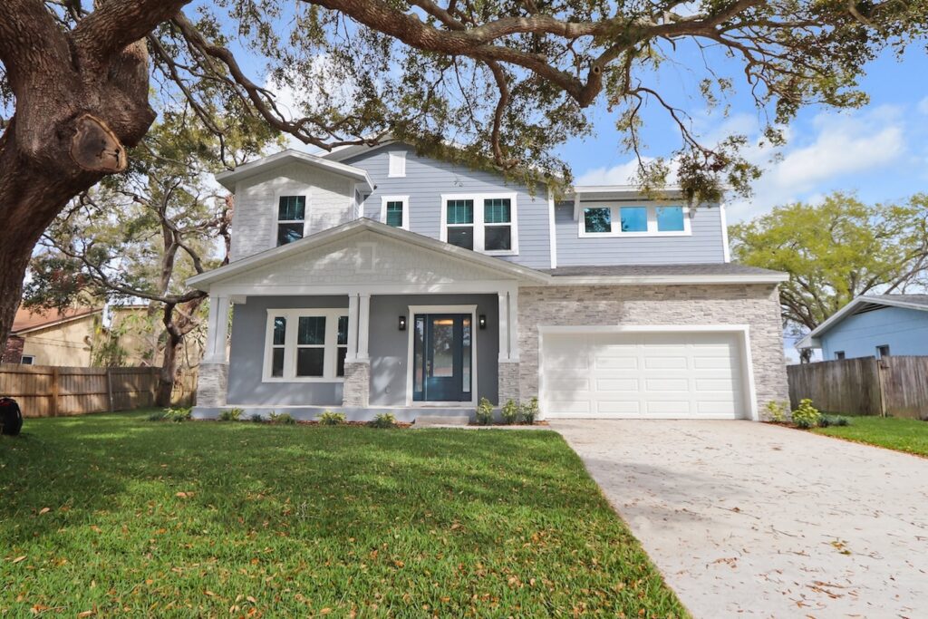 Exterior View of New Cottage Style Home by WinWay Homes in Pale Gray, White Trim, and Columned Porch with Stone Accents Under a Tree